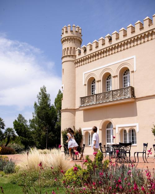 A tan castle-like building with two children on a patio.