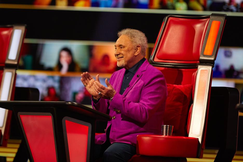 Sir Tom Jones, coach on The Voice UK, smiling and clapping in his red chair.