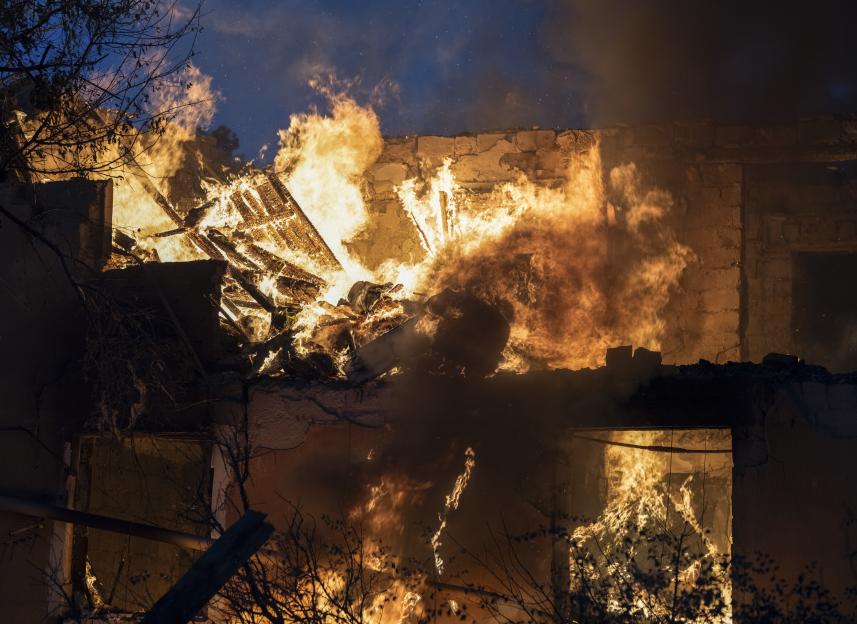 Flames and smoke engulf the interior of a building, with charred debris visible.