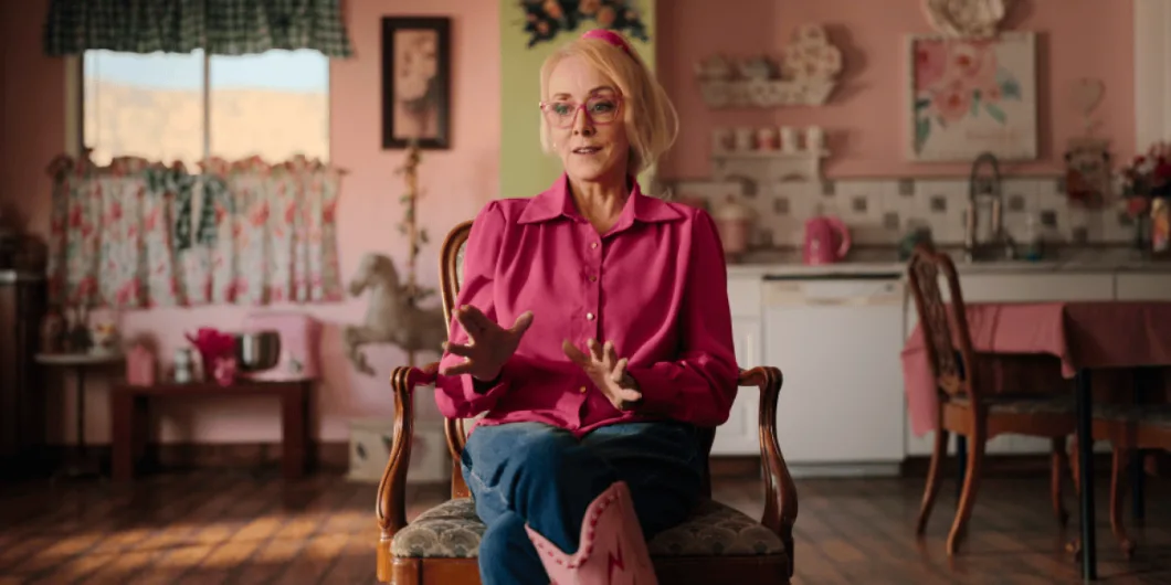 Christine Marie sits in a chair in a room with pink walls, gesturing with her hands while speaking.