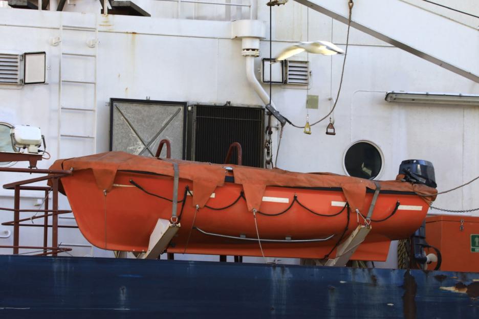 An orange lifeboat with a brown cover and black outboard motor mounted on a ship.