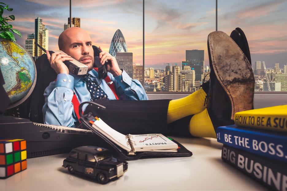 Illustration of a man in an office with his feet up on the desk, talking on a corded phone, with a city skyline in the background.