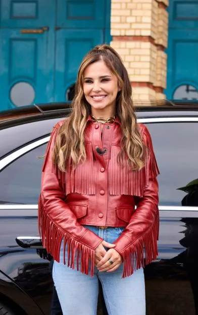 Cheryl wearing a red fringed jacket and jeans.