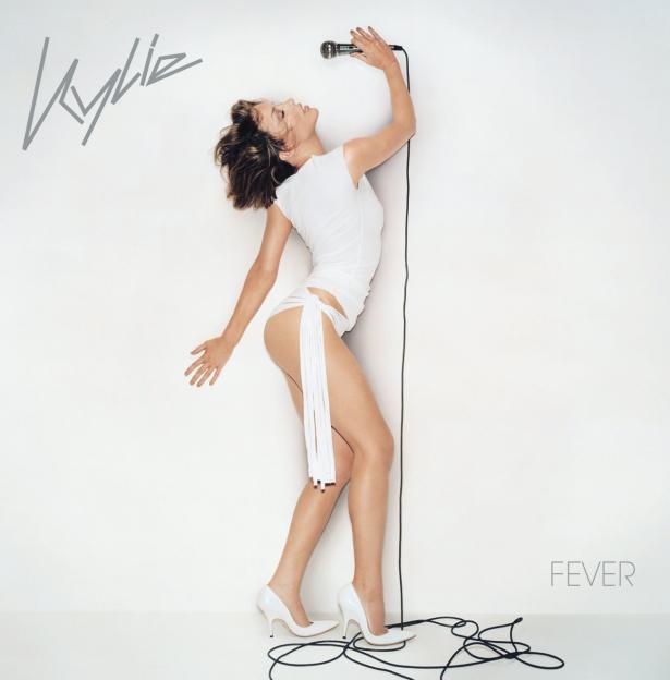 Kylie Minogue in white bodysuit with microphone, promoting "Fever" album.