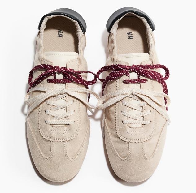 A pair of beige H&M sneakers with red and white patterned laces and cream laces.