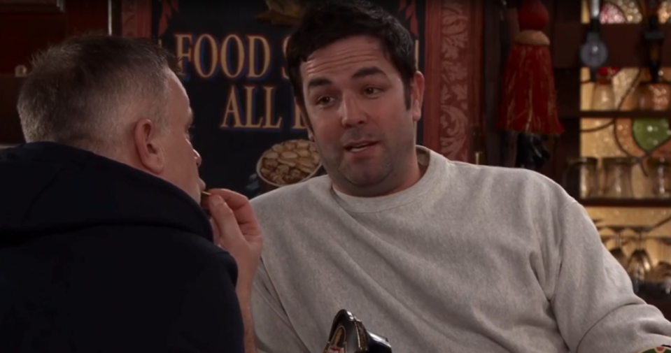 Two men, one with his back to the viewer, face each other in a dimly lit bar.