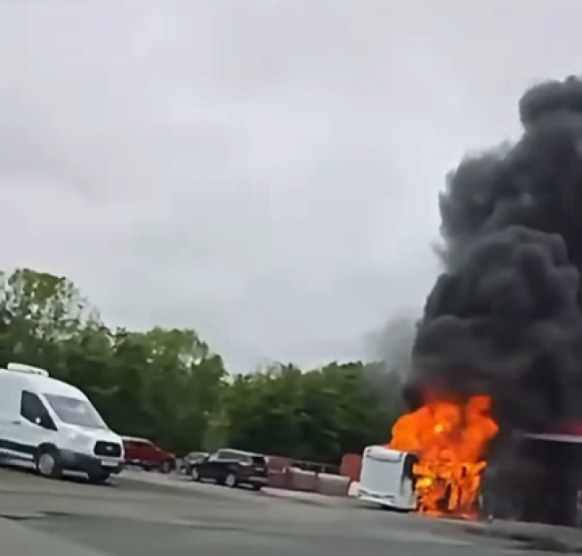 A campervan engulfed in flames and black smoke at a petrol station forecourt.