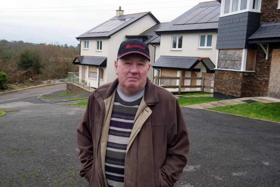 A man standing in front of an abandoned new-build housing estate with boarded-up windows.