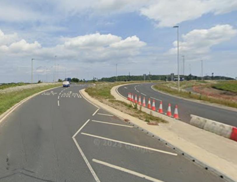A winding road with a car on the left lane and traffic cones lining the right side of the road.