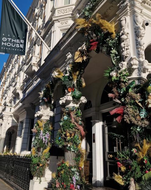 The entrance of The Other House Kensington, decorated with lush greenery, butterflies, and dried flowers.
