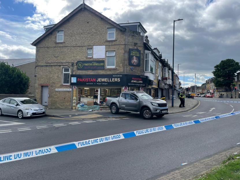 A silver pickup truck parked outside Pakistan Jewellers on Duckworth Lane in Bradford with the storefront glass shattered and police tape across the street.