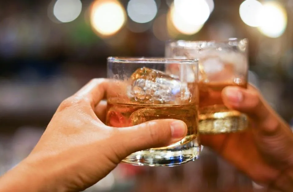 Two people clinking glasses of whiskey at a pub.