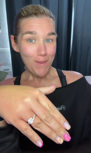 Woman with blue eyes shows off an engagement ring on her left hand.