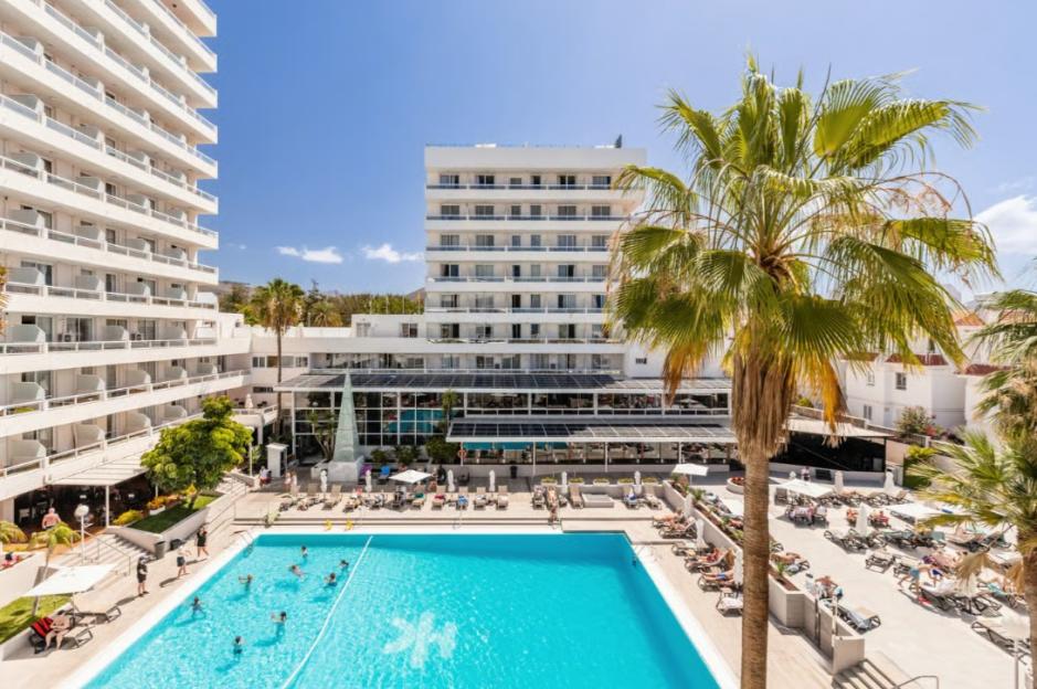 Holiday resort with a large swimming pool, two tall white buildings, and palm trees.