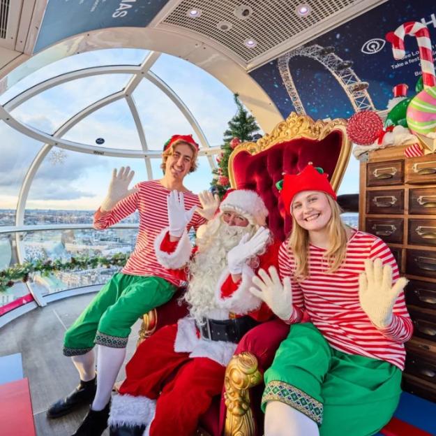 Santa Claus sitting on a red throne with two elves in a Ferris wheel pod.