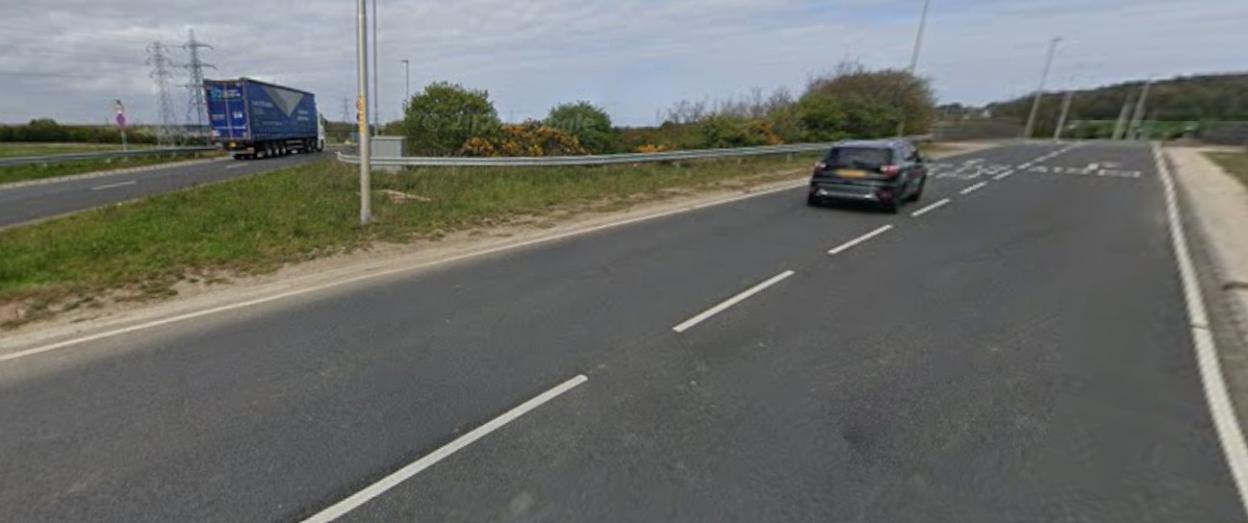 Road with a black car and a blue truck, with power lines and trees in the background.