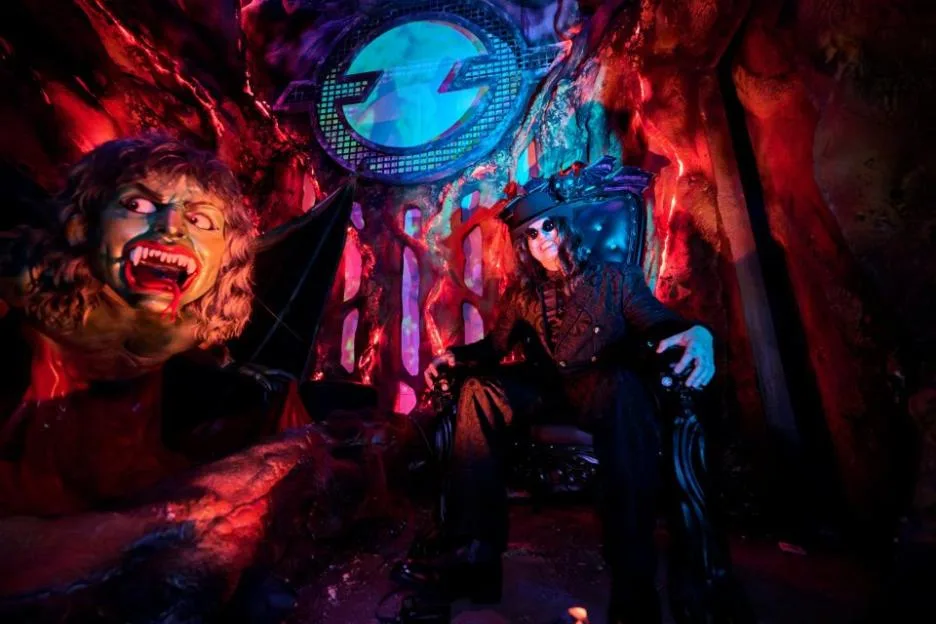 Ozzy Osbourne sitting on a throne next to a vampire monster in a dungeon-like setting with red and blue lighting.