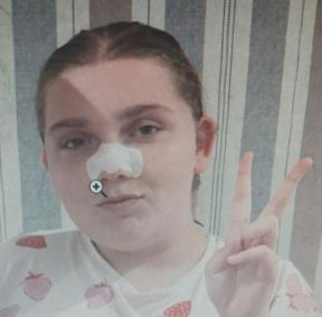 A young woman with a white patch on her nose making a peace sign.