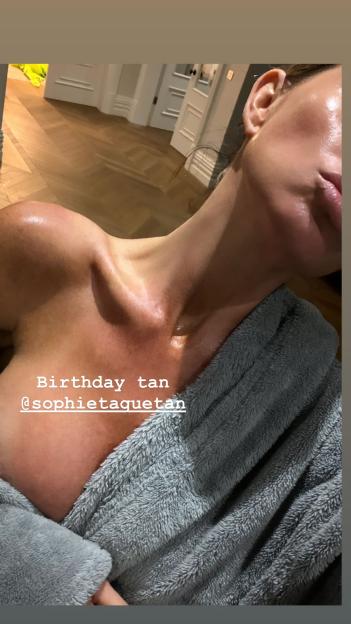 Abbey Clancy's tanned shoulders and chest in a grey bathrobe, with text "Birthday tan @sophietaquetan".
