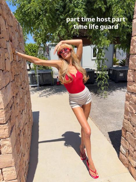 A woman in a red swimsuit and striped shorts posing next to a stone wall with text overlay "part time host, part time life guard".