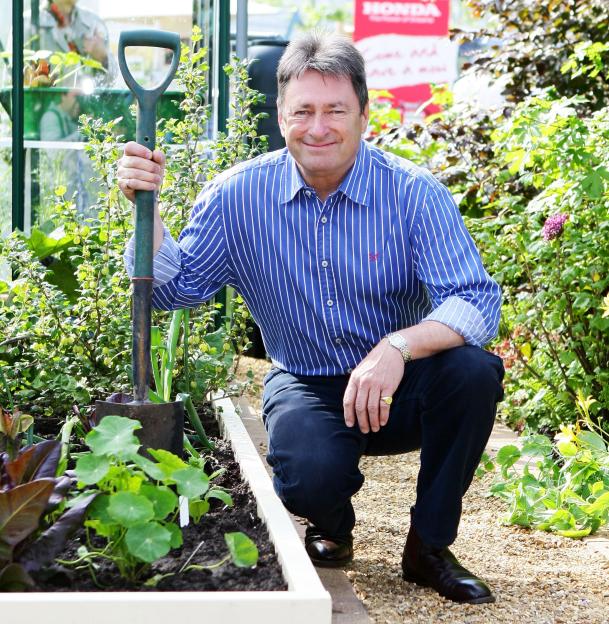 Alan Titchmarsh kneeling in a garden bed with a shovel.
