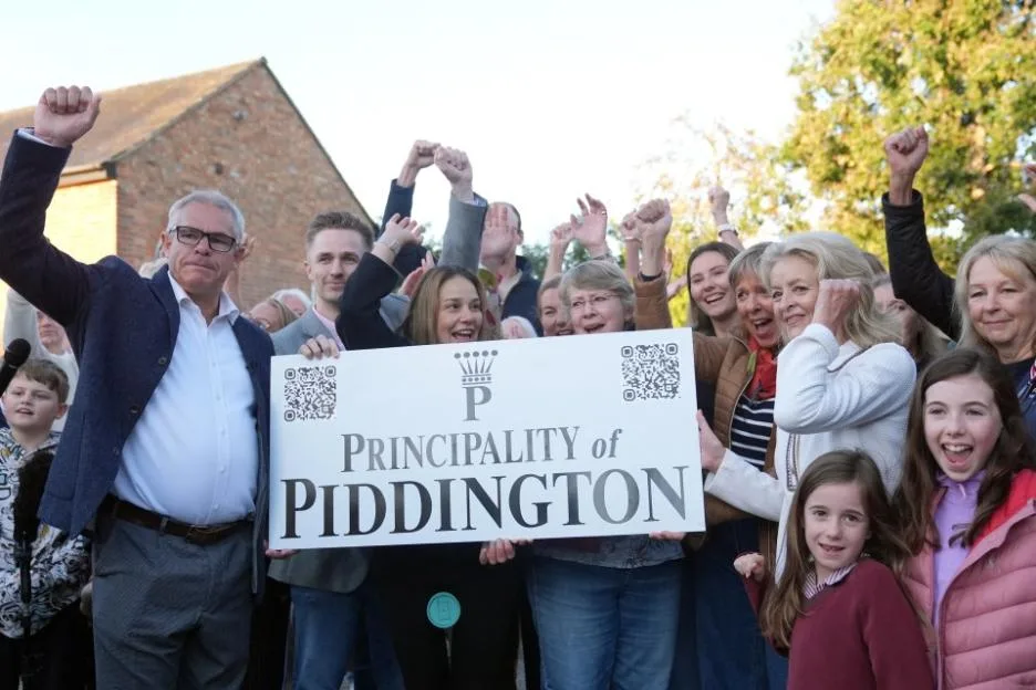 Residents of Piddington, Oxfordshire, cheering with a "Principality of Piddington" sign.
