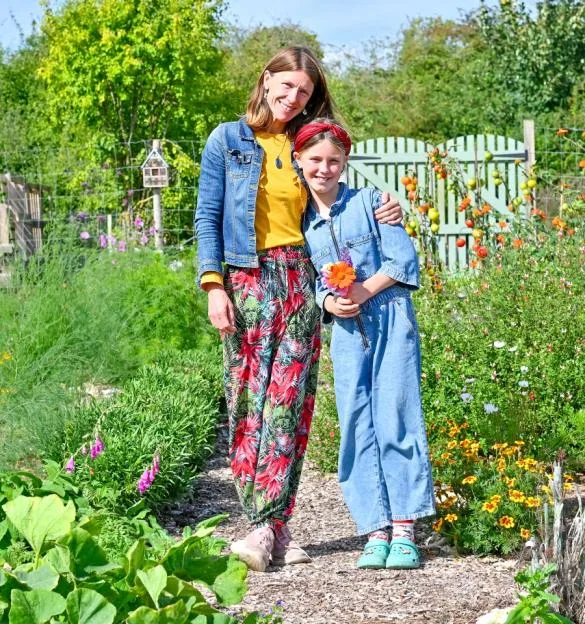 Holly Wright and her daughter stand together on a path in a lush garden at Jolly Moon.