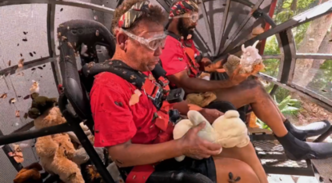 Two men in safety gear sitting in an enclosure filled with insects and stuffed animals.