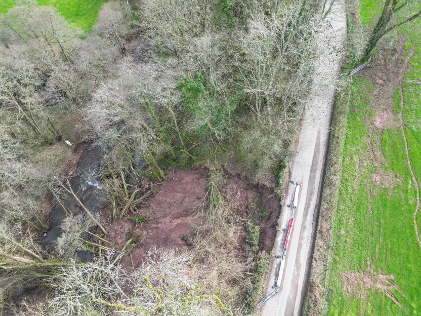 Aerial view of a landslip with trees, a small creek, and a road to the right.