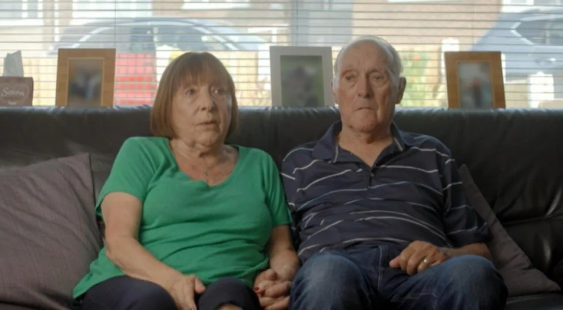 A couple sitting on a couch, holding hands.