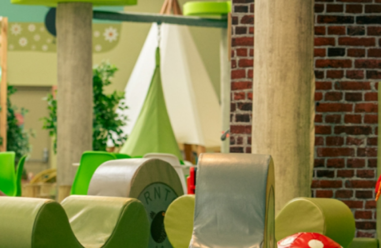 Soft play area for children with green and white structures, a green tent, and a brick wall.