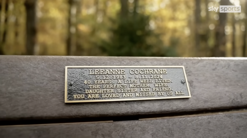 A bronze plaque memorializing Leeanne Cochrane (1983-2024) is affixed to a park bench.