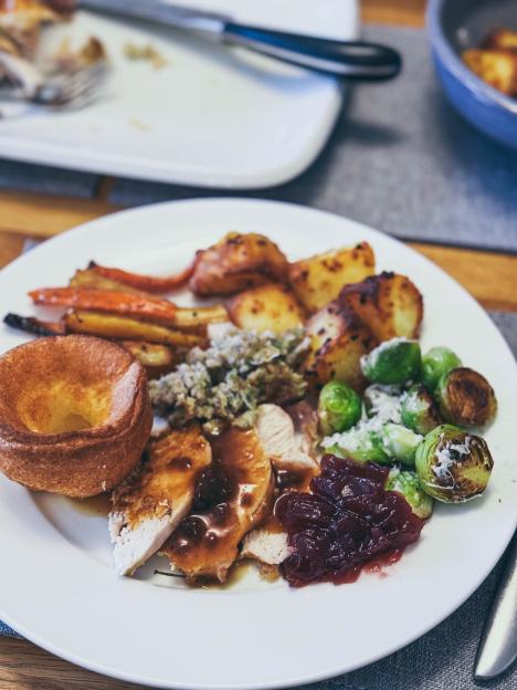 Festive Christmas dinner plate with sliced turkey, roasted potatoes, parsnips, carrots, Brussels sprouts, Yorkshire pudding, and cranberry sauce.