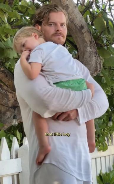 A man with a beard holds a sleeping child on his shoulder.