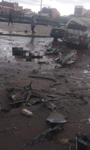 Debris from a disaster in a muddy, flooded street with damaged cars and a blurred out body.