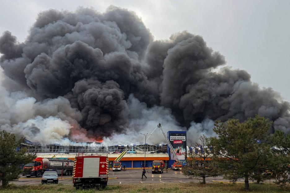 Building engulfed in flames and thick black smoke with firefighters battling the blaze.