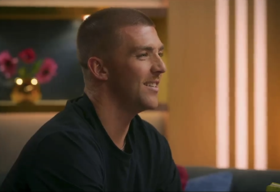 A man with short hair smiles, looking to his right.