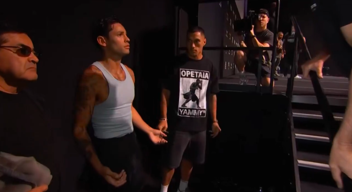 Three men stand near a dark set of stairs while another man films them.