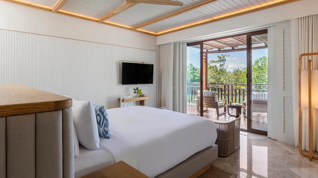 A luxury hotel room at Fairmont Mayakoba with a king-sized bed, television, and a balcony overlooking a lush landscape.