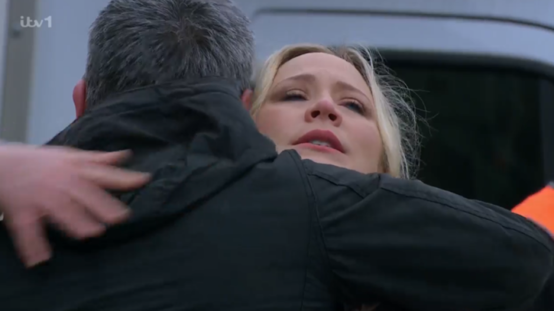 A distraught blonde woman with tears in her eyes hugs a man.