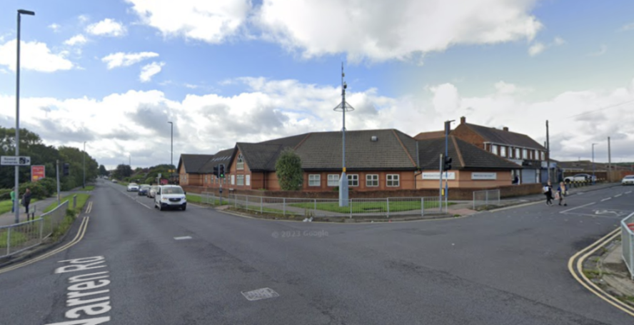 Street view of a road intersection with brick buildings, traffic, and pedestrians.