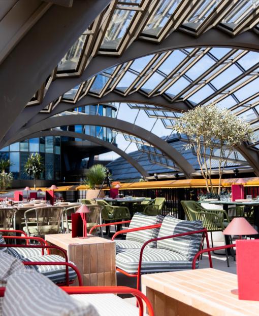 A bar or restaurant with red-framed chairs and tables under a glass ceiling.