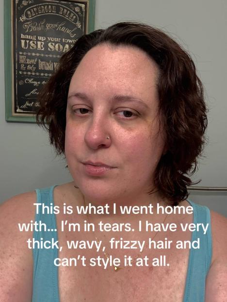 A woman with dark, frizzy hair, wearing a teal tank top and a gold necklace, looks sadly at the camera.