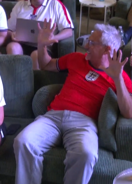 Man in red England football shirt gesturing with his hands.