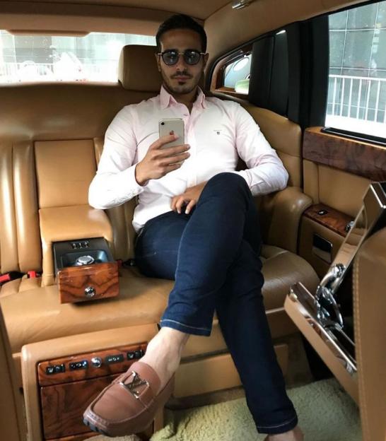 Shimon Hayut, the Tinder Swindler, in the back of a luxury car holding his iPhone.