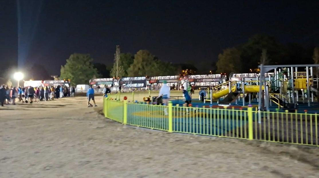 A night shot of a playground area with a crowd of people in the background.