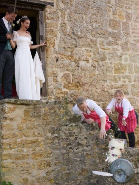 A bride and groom react in shock as a wedding cake tumbles down stone steps.