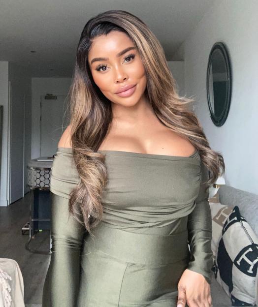 A woman with long wavy brown hair and highlights wearing a green off-the-shoulder top.