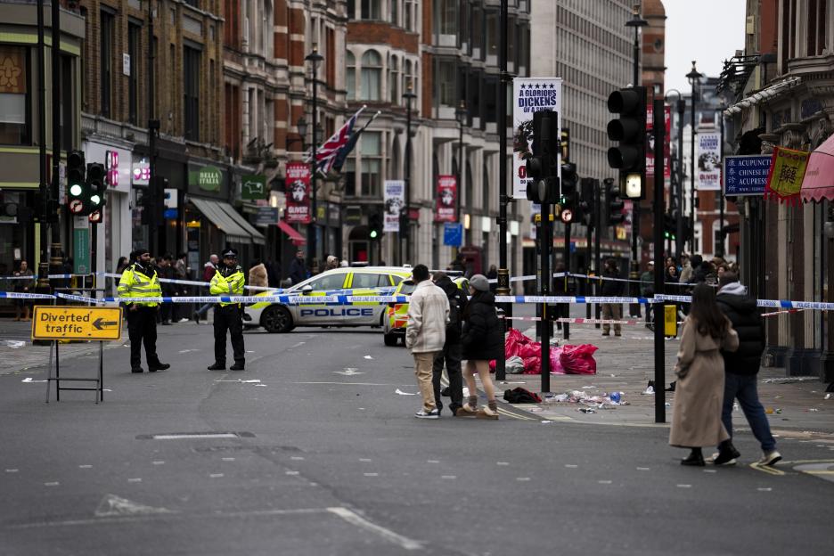 Police at a crime scene on Shaftesbury Avenue in Central London, marked off with "Police Line Do Not Cross" tape, with a police car visible and a "Diverted traffic" sign in the foreground.