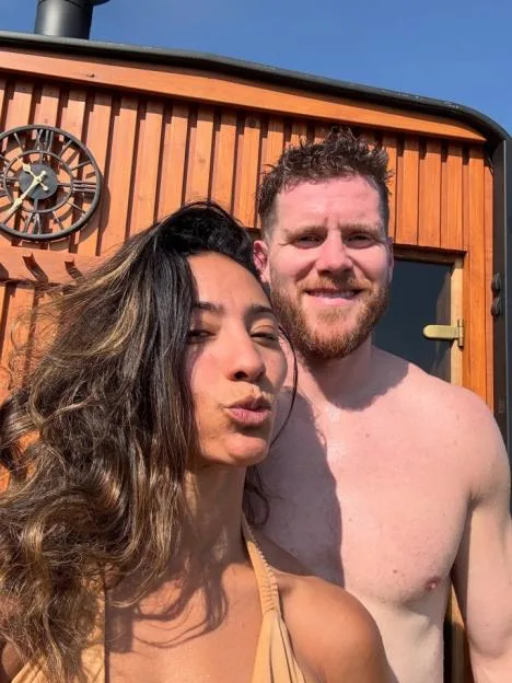 Karen Hauer and her boyfriend pose for a selfie in front of a wooden building.